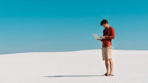 freelancer on sandy beach with laptop against clear blue sky